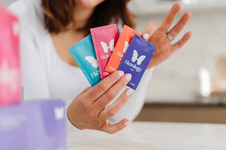 Person holding  packets with 'Herology' branding