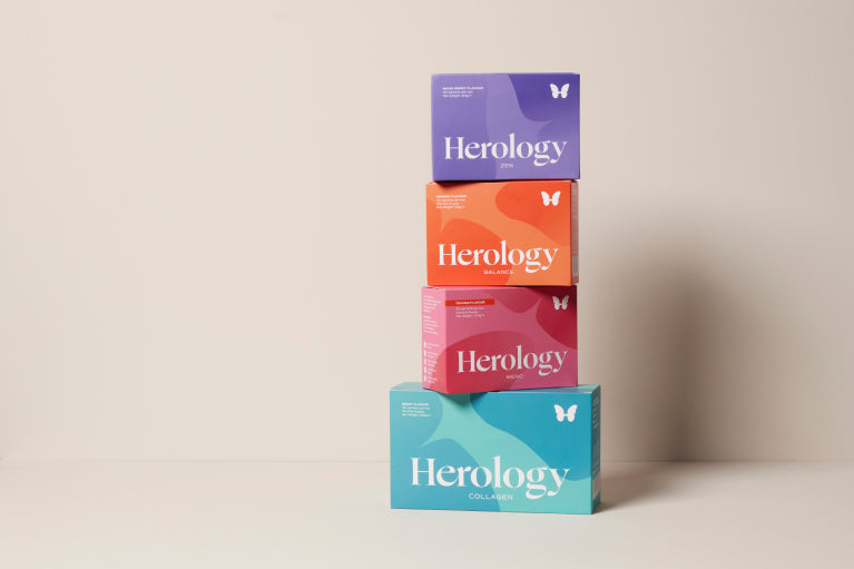 Four 'Herology' product boxes stacked on a light beige background
